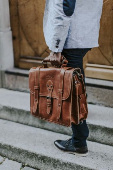 Brauner Lederrucksack wird von einer Person in einem Anzug getragen.